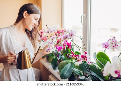 Woman Taking Care Of Orchids Blooming On Window Sill. Girl Gardener Watering Home Plants And Flowers With Watering Can.