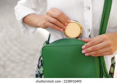 Woman taking cosmetic pocket mirror from bag outdoors, closeup