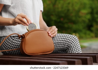Woman taking cosmetic pocket mirror from bag on bench outdoors, closeup