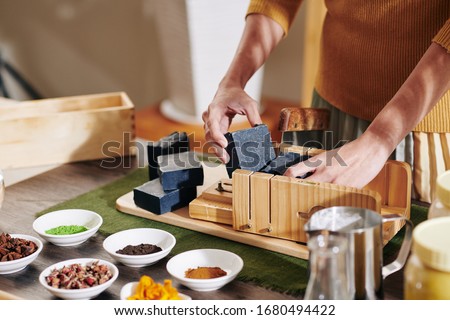 Woman taking cut black soap bar out of adjustable wooden mold