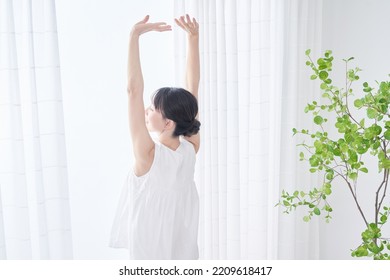 A woman taking a deep breath by a bright window - Powered by Shutterstock