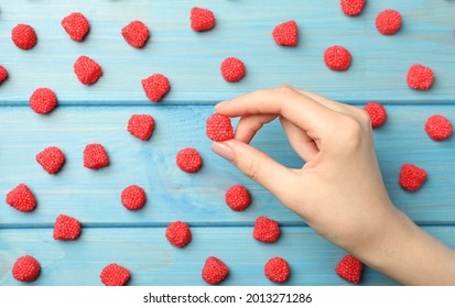 Woman Taking Delicious Gummy Raspberry Candy At Light Blue Wooden Table, Top View