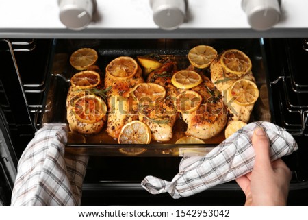 Woman taking delicious lemon chicken out of oven, closeup