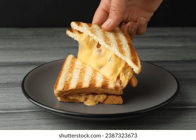 Woman taking delicious sandwich with ham and melted cheese at grey wooden table, closeup - Powered by Shutterstock