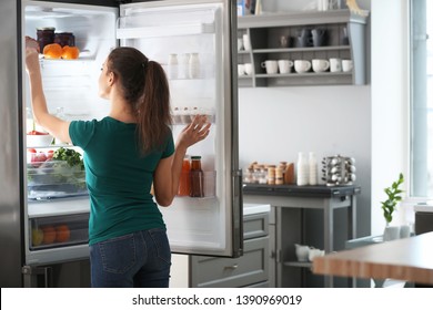 Woman taking food out of fridge at home - Shutterstock ID 1390969019