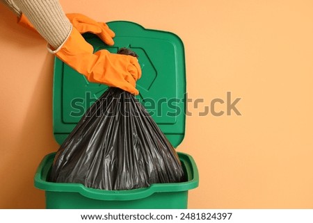 Woman taking garbage bag from trash bin near orange wall, closeup