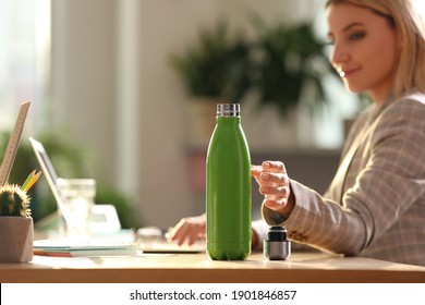 Woman taking green thermos bottle at workplace, closeup