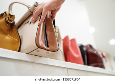 Женщина берет свою любимую сумочку из коллекции дорогих модных сумок, стоящих на полке