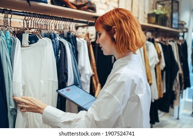 Woman Taking Inventory On Digital Tablet In Clothing Store. Woman Manager In A Fashion Retail Store Using A Tablet For Working And Checking The Shop Stock.