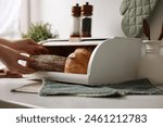 Woman taking loaf from wooden bread basket at white marble table in kitchen, closeup