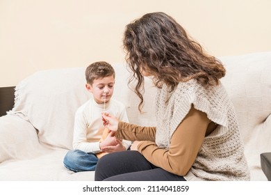 Woman Taking A Nasal Swab From A Child, Seated On A Sofa, To Perform A Covid19 Antigen Test At Home.