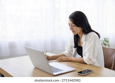 Woman Taking Notes While Working on Laptop at Desk