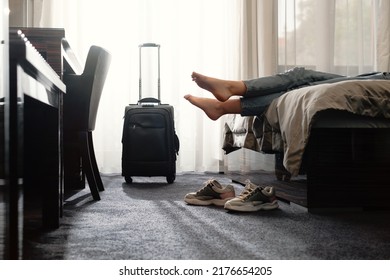 woman taking off footwear in a hotel room on the bed. Tourist relaxing on hotel room after travelling with suitcase. Female having rest after long trip with language Dark silhouette  - Shutterstock ID 2176654205
