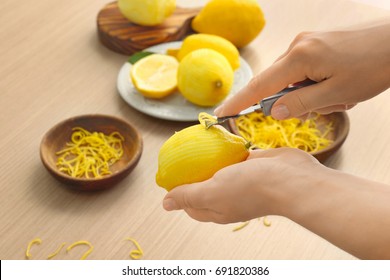 Woman taking off lemon peel with zester over table - Powered by Shutterstock