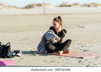 Woman Taking Off The Sweater While Sitting On A Yoga Mat On A Beach