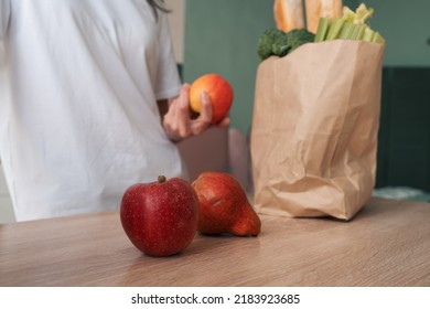 Woman Taking Out Fresh Fruits Of A Shopping Paper Bag On Kitchen Table Before Prepare Cooking Healthy Food