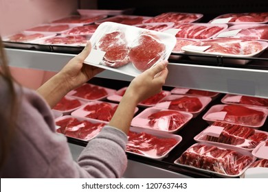 Woman taking packed pork meat from shelf in supermarket - Powered by Shutterstock