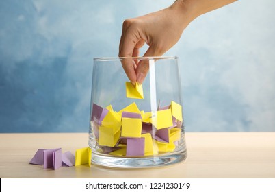 Woman taking paper piece from glass vase on table. Lottery