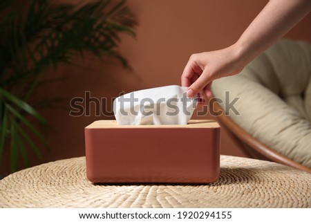 Woman taking paper tissue out of box on table indoors, closeup