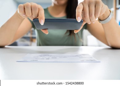 Woman Taking Photo Of Cheque To Make Remote Deposit In Bank