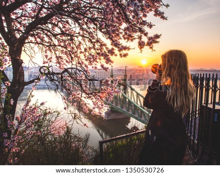 Woman taking photo the cityscape and the Liberty bridge over Danube from the terrace of the Gellert hill in Budapest, Hungary on sunrise
