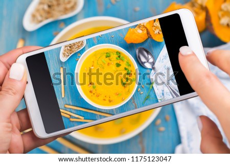 Woman taking photo of fall spicy pumpkin soup with herbs, croutons and sunflower seeds. Trendy instagram photo shot. Top view, flat lay style. Copy space