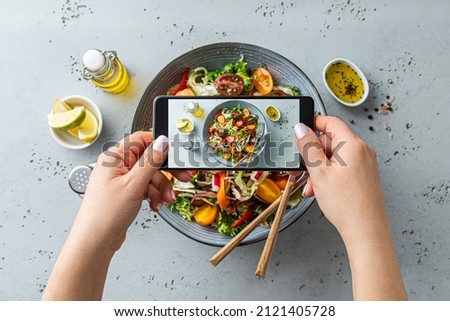Woman taking photo of fresh, spring, vegetable salad with smartphone. Using phone while eating lunch. Lifestyle trend - posting and sharing food pictures (images) on social media.