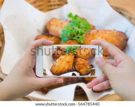woman taking photo of hot and spicy chicken wings in basket with mobile smartphone