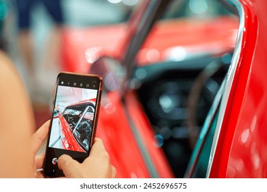 A woman is taking a photo of an old vinatge red car with her mobile phone, so she can share it on social media.