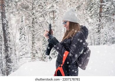 Woman taking photo on phone in snowy winter forest, snowy winter day