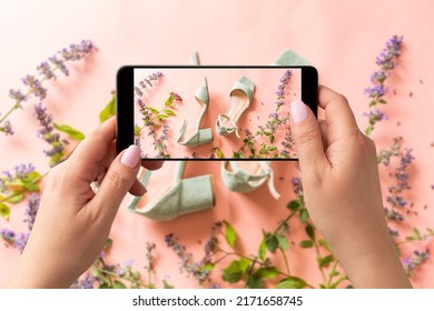 Woman Taking Photo Of Pastel Mint Green Sandals Shoes And Meadow Flowers With Smartphone. Blogger, Influencer Or Stylist Capturing Fashion Footwear For Social Media. Pink Background.