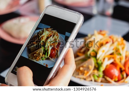 Woman taking a photo of thai green papaya salad with smartphone