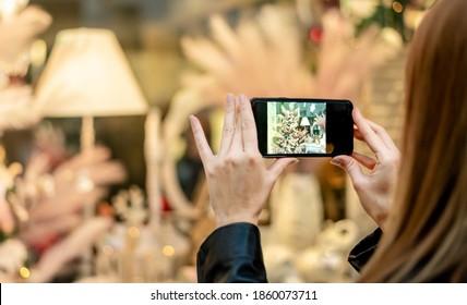 Woman Taking Picture Of Beautiful Christmas Store Window Display With Her Smartphone.