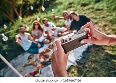 Woman taking picture of her friends by vintage camera on picnic at summer park. Selective focus - Powered by Shutterstock