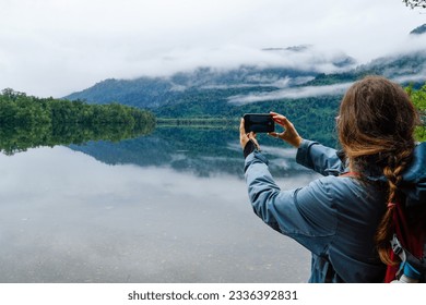 A woman taking a picture with her smart phone in a beautiful lagoon in the south of Chile