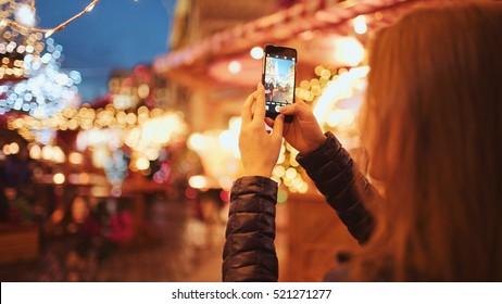 Woman Taking Pictures of European Christmas Market Scene on Smartphone. 4K. Girl Enjoying Winter Holiday Season, visiting Outdoors Christmas Market, Making photos on cell phone. Travel Europe - Powered by Shutterstock