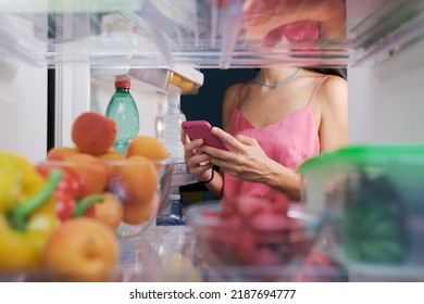 Woman Taking Pictures Of Food In The Fridge Using Her Smartphone, POV Shot From Inside Of The Fridge