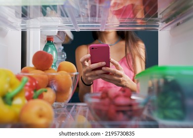 Woman Taking Pictures Of Food In The Fridge Using Her Smartphone, POV Shot From Inside Of The Fridge