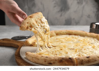 Woman taking piece of delicious cheese pizza at light grey table, closeup - Powered by Shutterstock