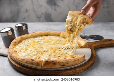 Woman taking piece of delicious cheese pizza at light grey table, closeup - Powered by Shutterstock