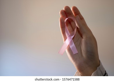 Woman Taking A Pink Ribbon On A Pink And White Background. Ribbon In Tribute To Breast Cancer Patients.