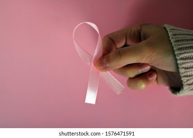 Woman Taking A Pink Ribbon On A Pink And White Background. Ribbon In Tribute To Breast Cancer Patients.