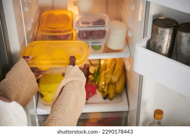 Woman taking plastic container with fresh fruits from fridge