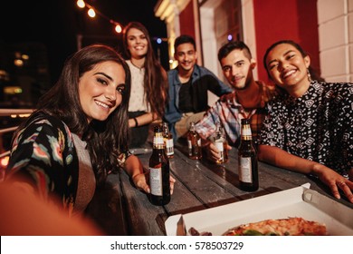 Woman taking selfie with friends at rooftop party. Group of young people having party at night.