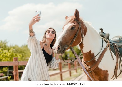 woman taking selfie on a phone with a horse on a ranch - Powered by Shutterstock