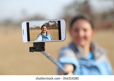 Woman Taking A Selfie Photo With Her Mobile Phone, Using A Selfie Stick. 