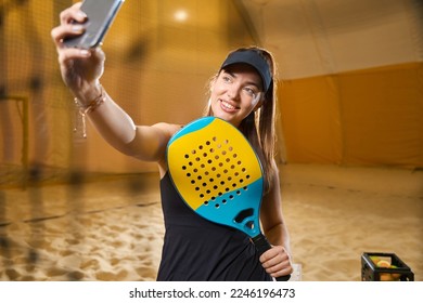 Woman taking selfie with smartphone while playing beach tennis indoors - Powered by Shutterstock