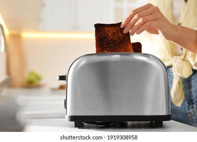 Woman Taking Slice Of Burnt Bread From Toaster In Kitchen, Closeup