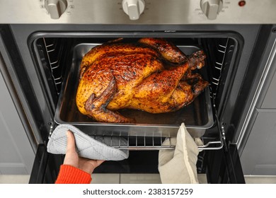 Woman taking tasty baked turkey from oven in kitchen. Thanksgiving Day celebration - Powered by Shutterstock