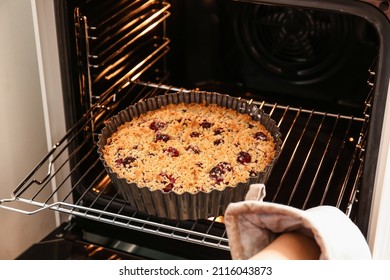Woman taking tasty cherry pie out of oven - Shutterstock ID 2116043873